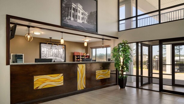 A reception area with a wooden counter, framed artwork, and a large window offering a view of the outdoors. - Super 8 by Wyndham Ocean Springs Biloxi (Ocean Springs)