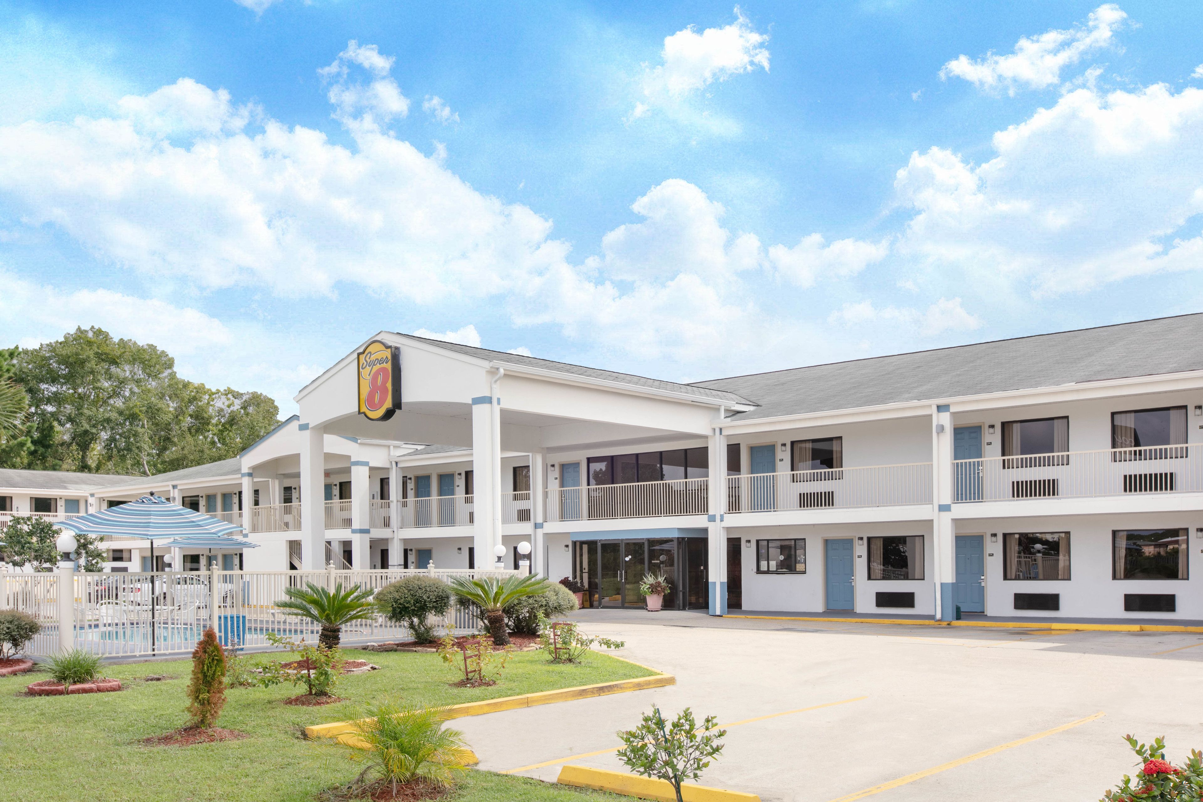 A motel with a central entrance, multiple balconies, and a swimming pool area.