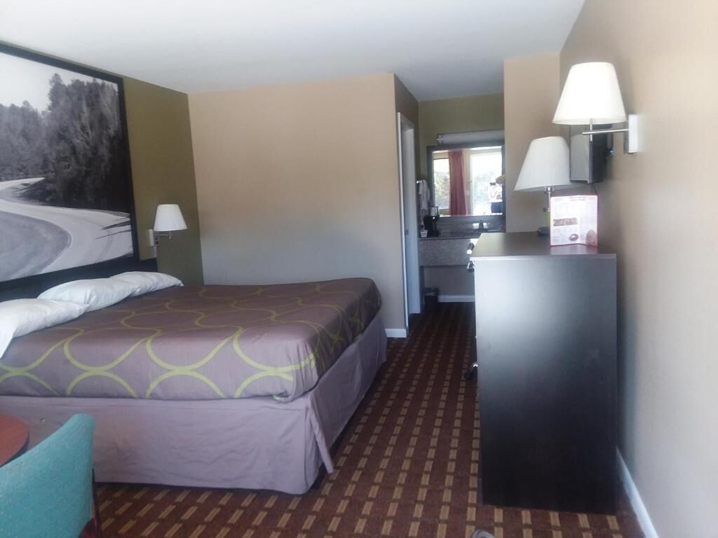 A hotel room with a bed, a desk, a lamp, and a painting on the wall.