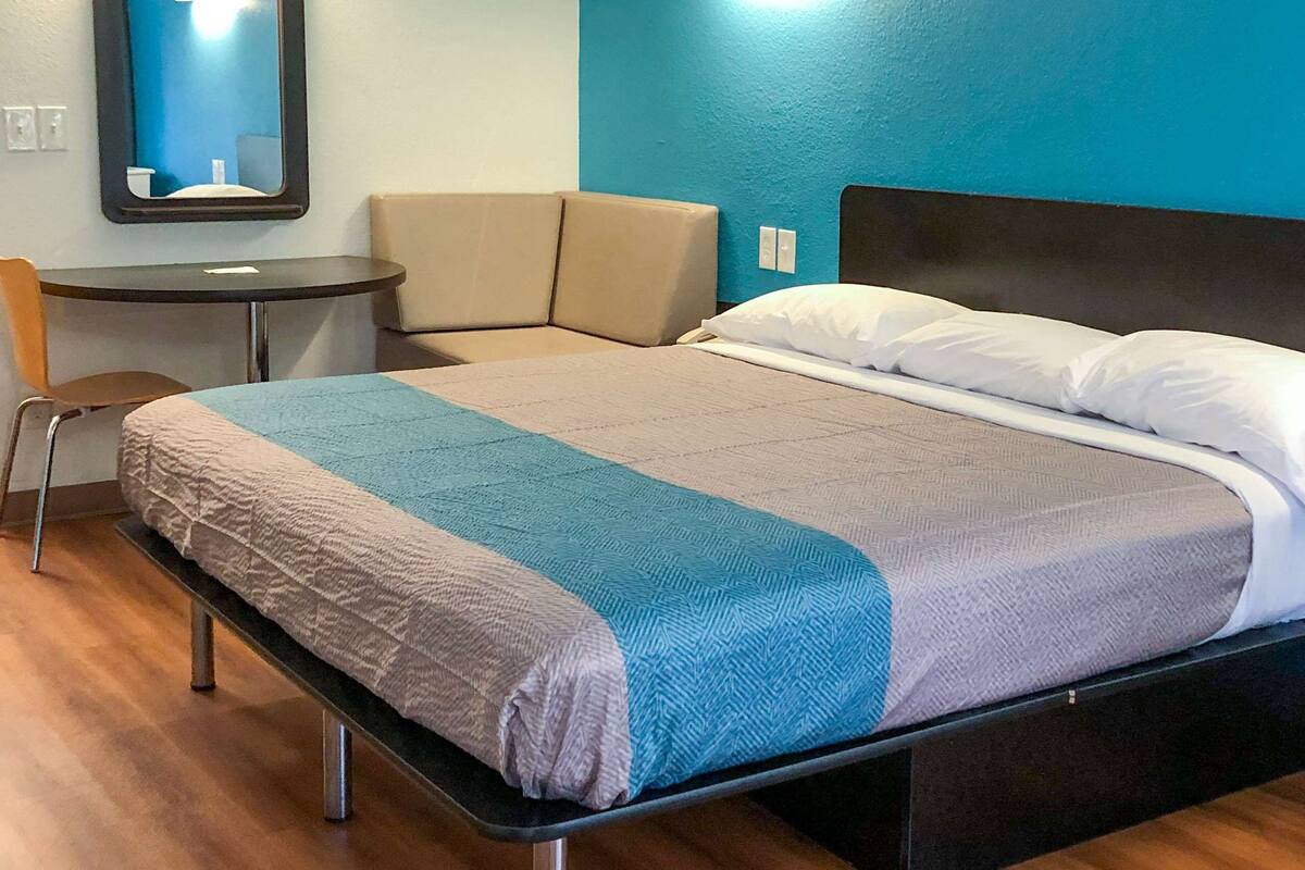 A hotel room with a bed, a chair, a small table, and a mirror.