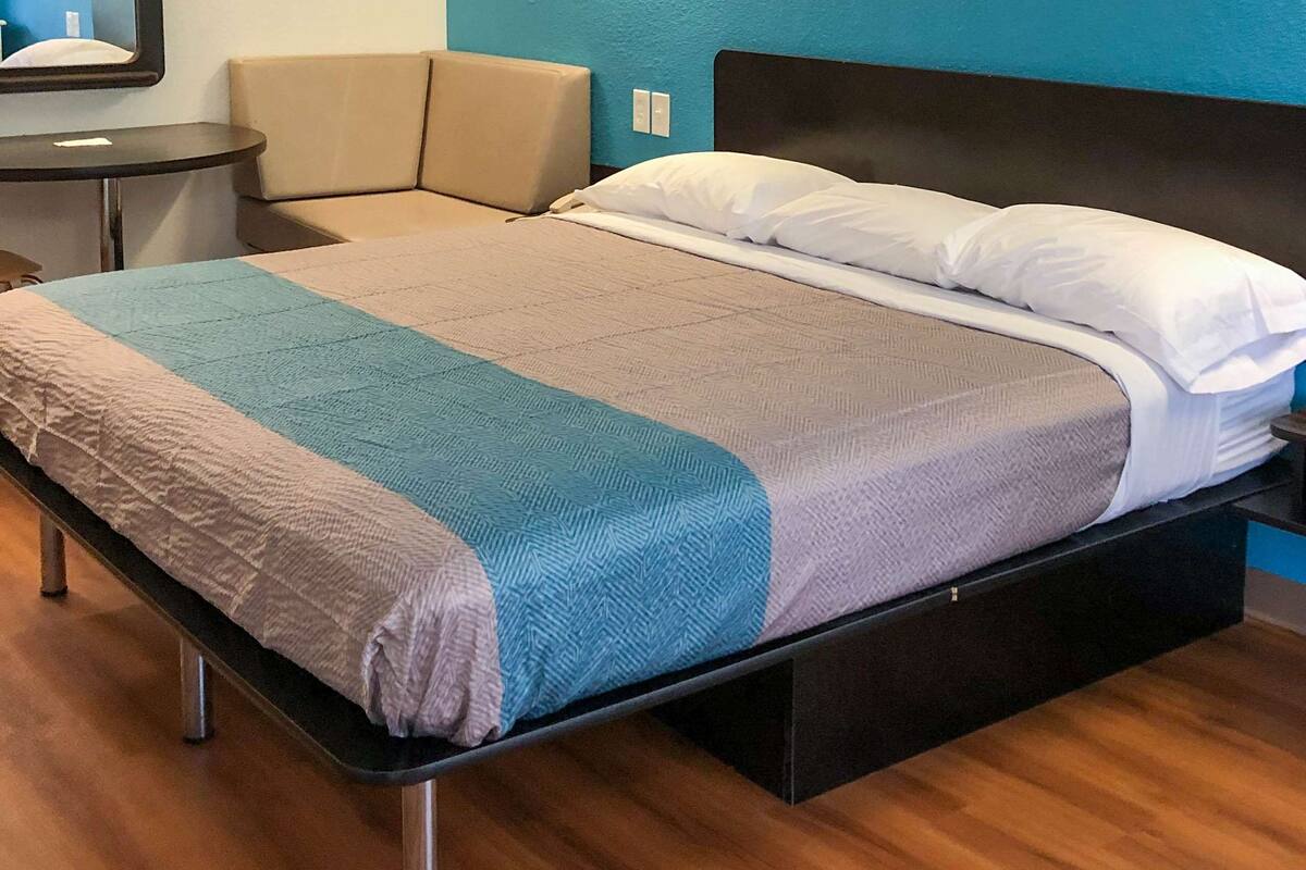 A bed with a grey and blue blanket, a white pillow, and a black headboard.