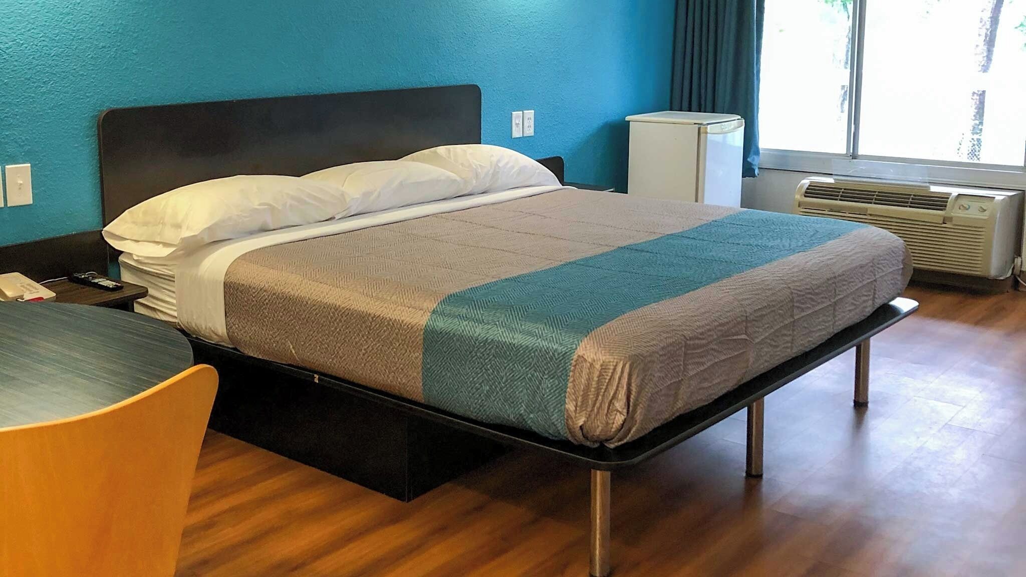 A single bed with a headboard, a bedside table, a chair, and a window with curtains.