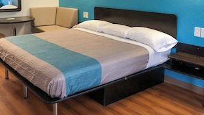 Una cama con cajón, una mesita de noche, una silla y una pequeña mesa con espejo.