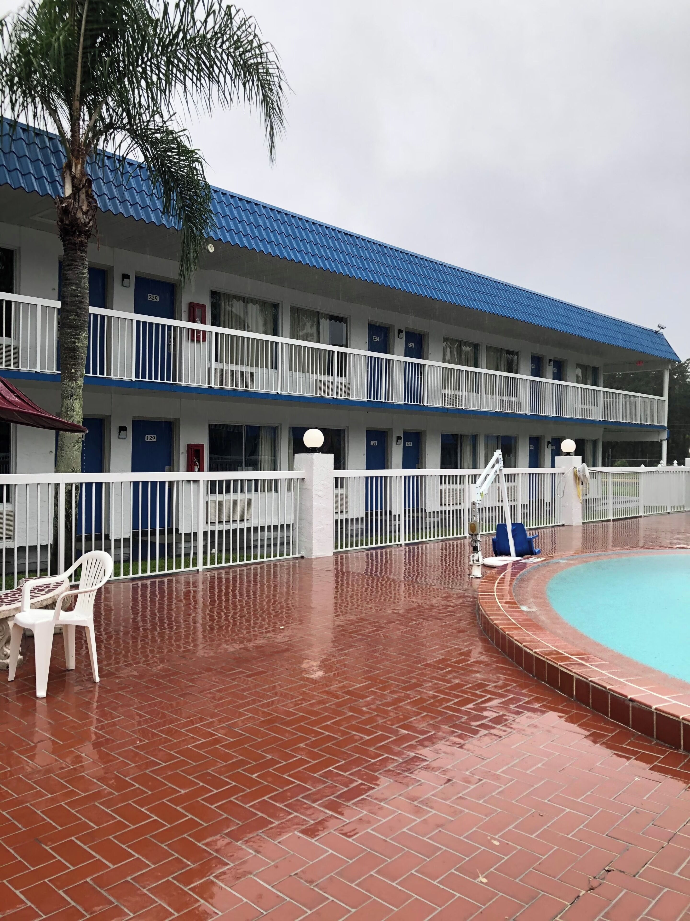 A multi-story motel with a blue roof, a swimming pool, and a palm tree.