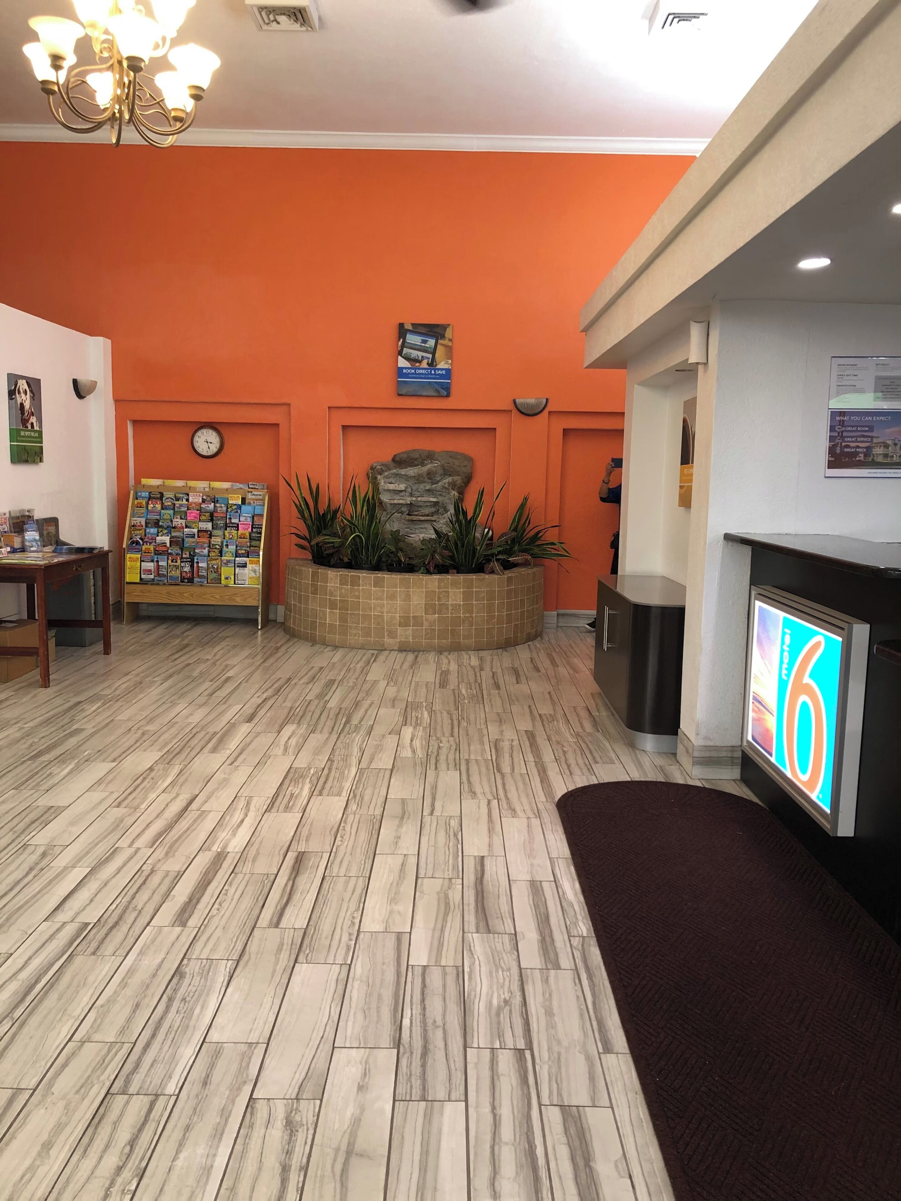 Un'area reception con una sveglia, una bacheca, un'esposizione di piante e uno schermo digitale.