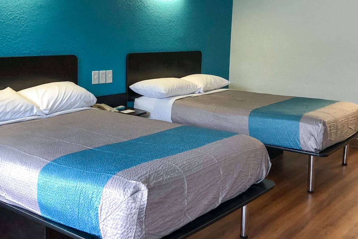 Two twin beds with grey and blue bedding, a wooden floor, and a teal wall.