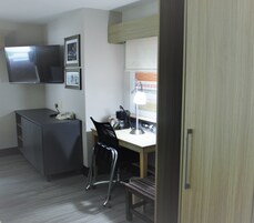 A compact hotel room with a desk, chair, and a TV mounted on the wall.