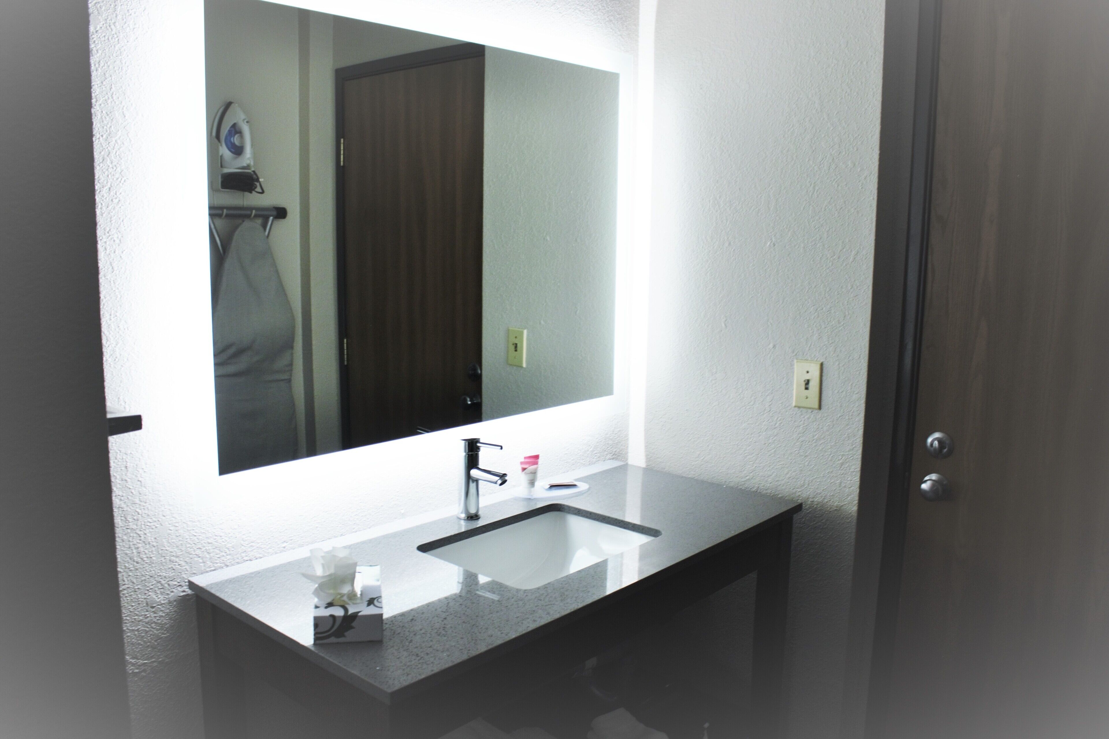 A bathroom with a large mirror, a sink, and a door.