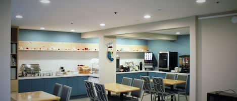 Une cuisine moderne avec des meubles bleus, une table en bois et quatre chaises. On trouve un four à micro-ondes et une machine à café sur le plan de travail.