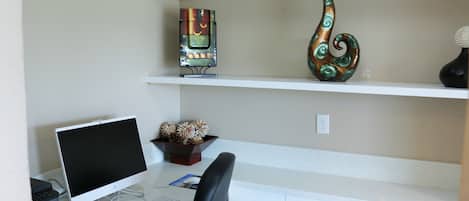 A desk with a computer, keyboard, and a chair. There are decorative items on shelves above the desk.