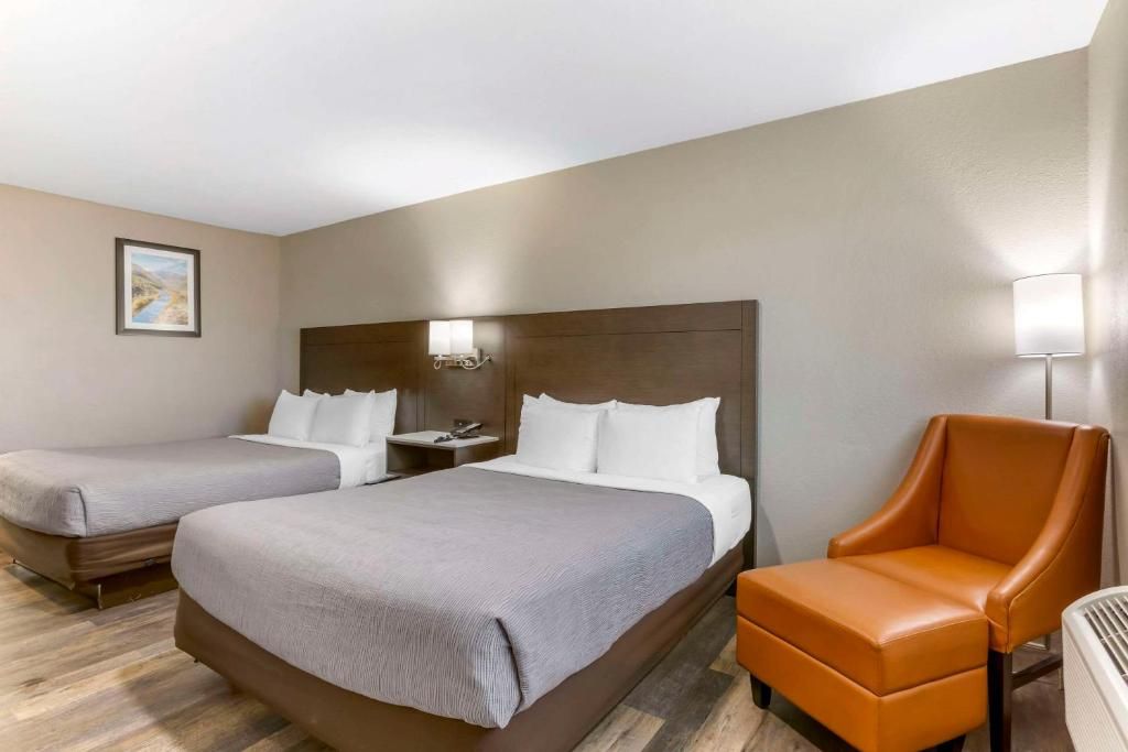 A hotel room with two beds, a nightstand, a lamp, and a chair.