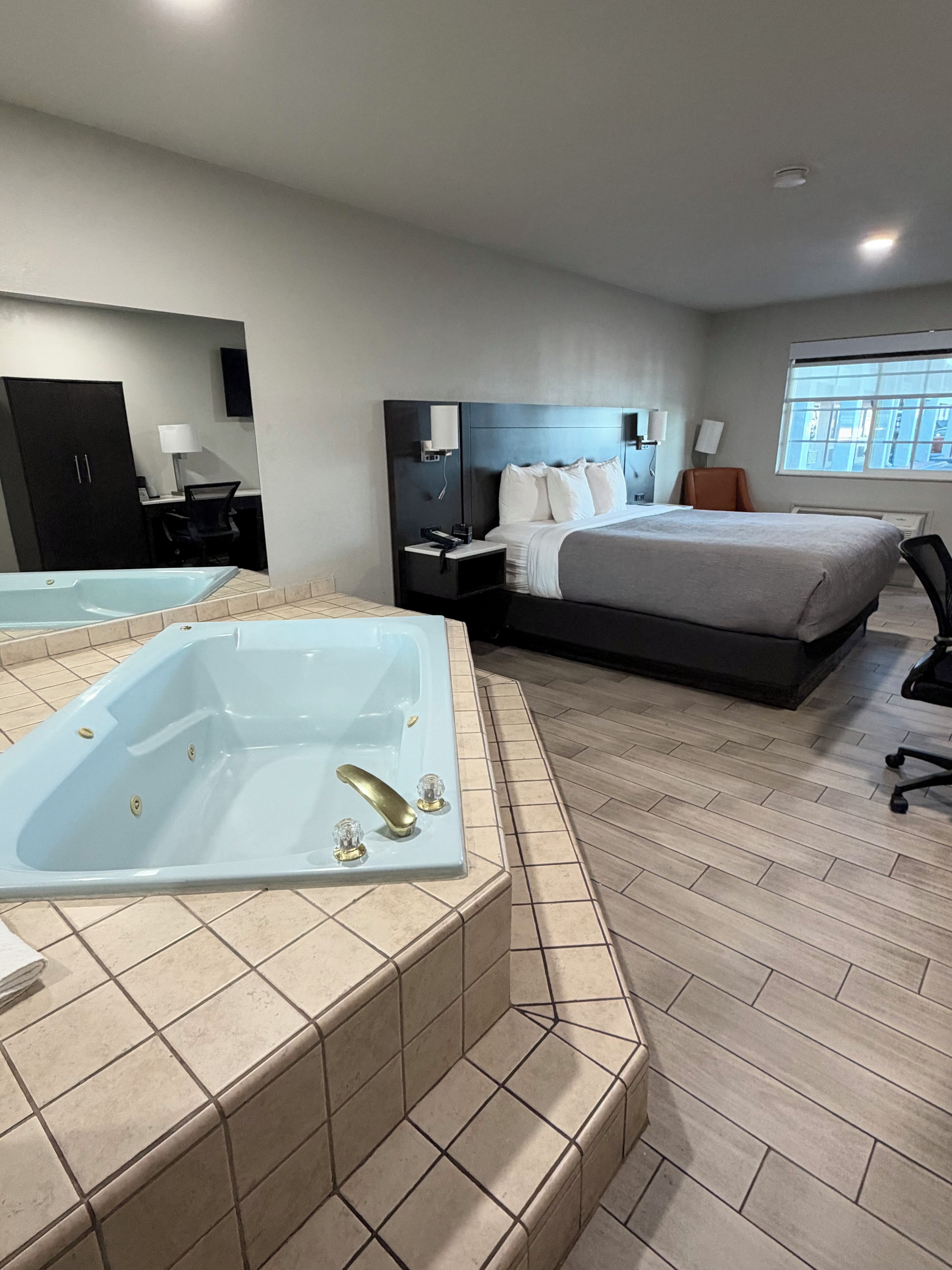 A modern hotel room with a large bed, a separate sitting area, a desk, and a separate bathroom with a bathtub.