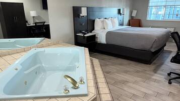 A modern hotel room with a large bed, a separate sitting area, a desk, and a separate bathroom with a bathtub.