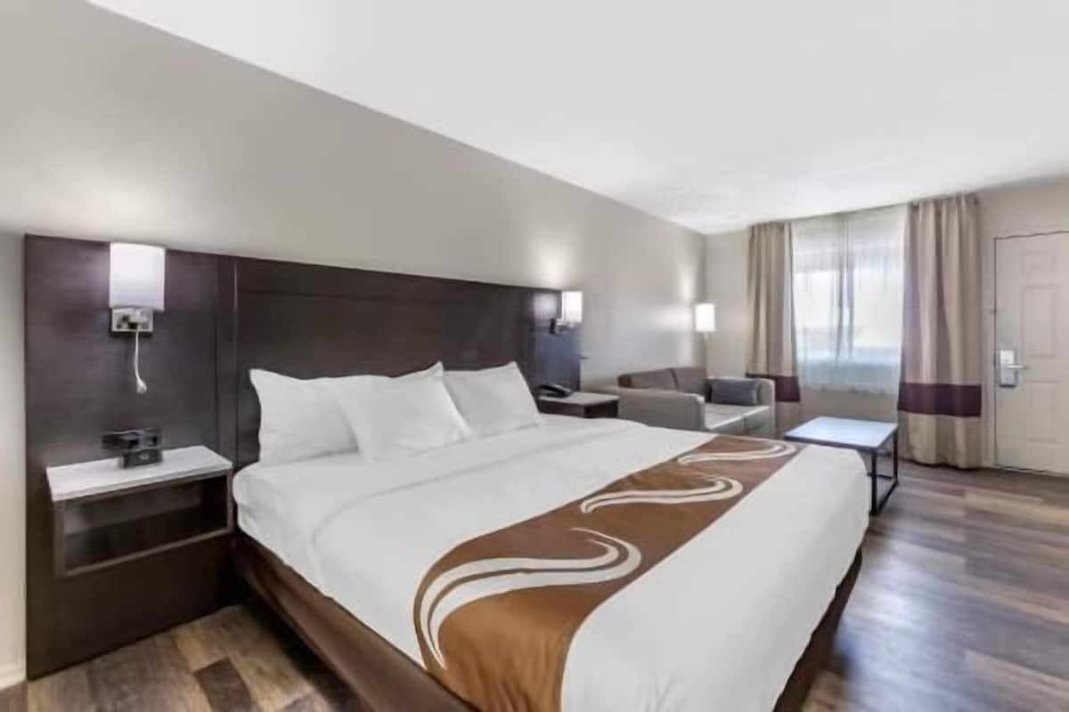 A hotel room with a large bed, bedside tables, a desk, a chair, and a view of the outside.