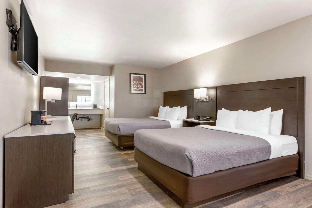 Habitación de hotel con dos camas, un escritorio, un televisor y un espejo.