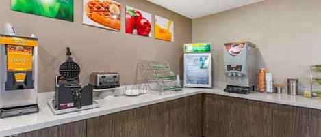 A breakfast bar with waffle, coffee, and juice dispensers, and a refrigerator.
