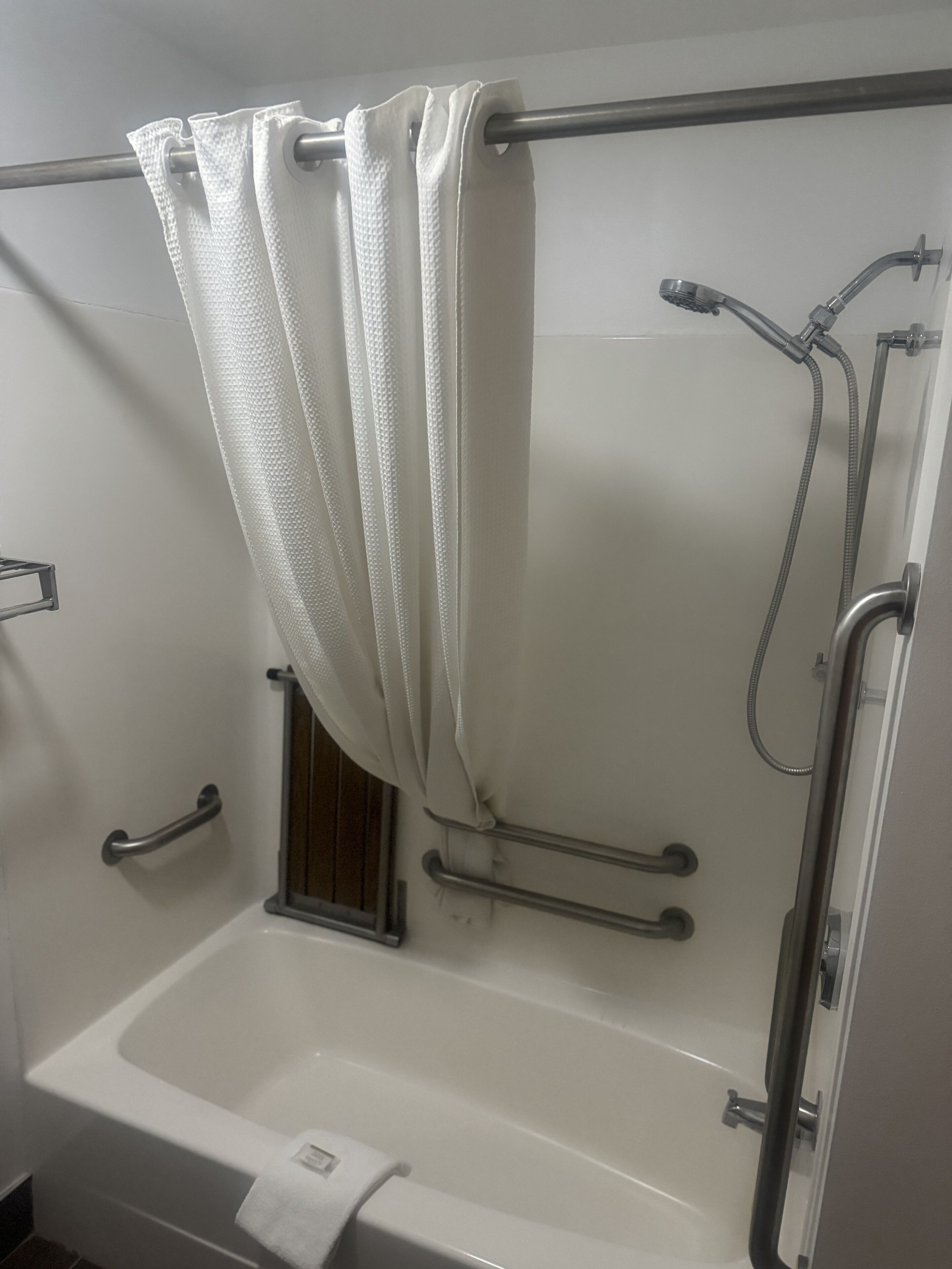A standard bathroom with a bathtub, shower, grab bars, and a towel rack.