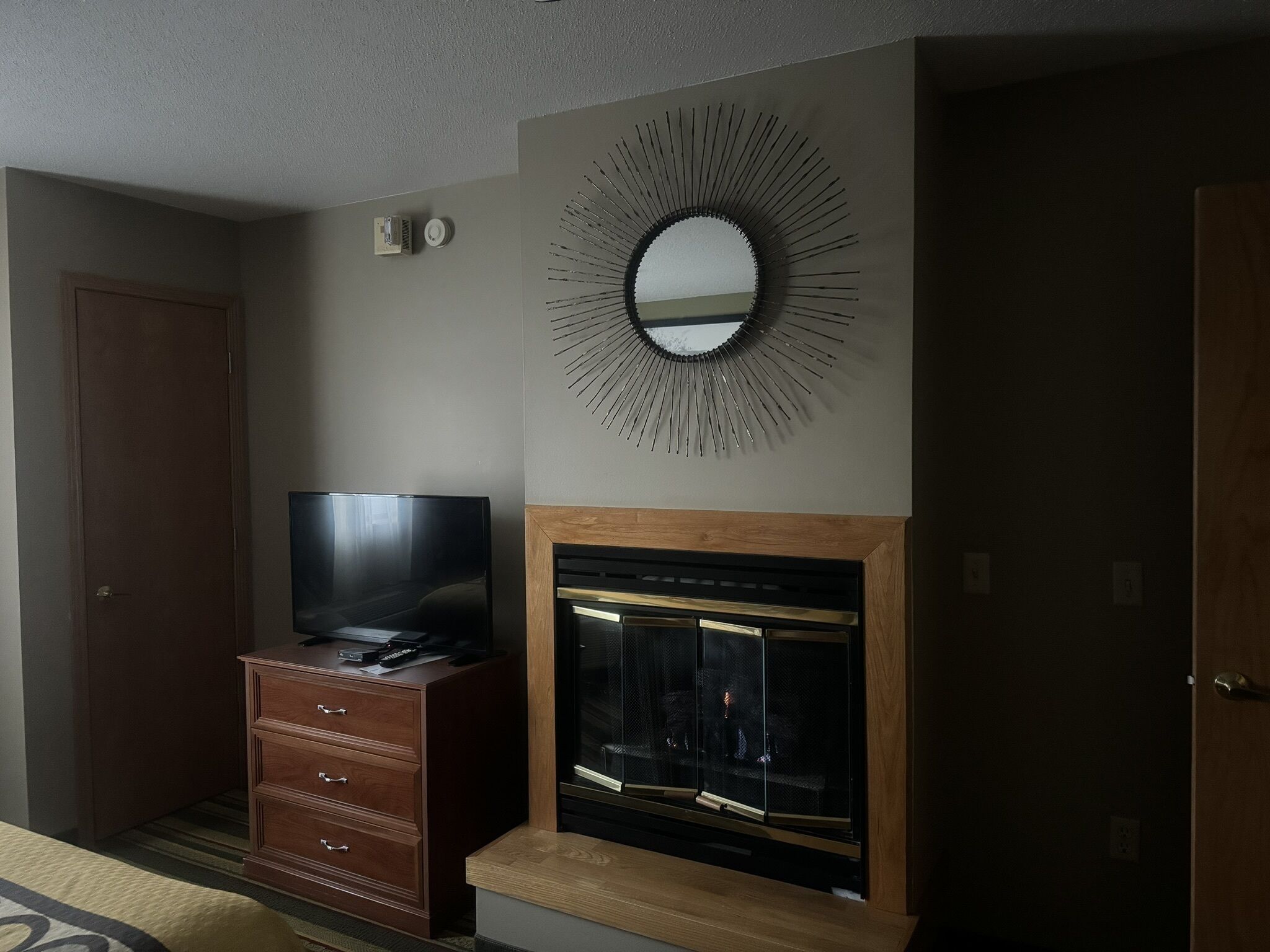 A hotel room with a TV on a wooden dresser, a fireplace, and a wall-mounted mirror.