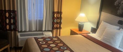 Una habitación de hotel con cama, escritorio, lámpara y ventana con cortinas.
