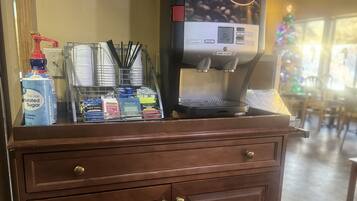 A coffee machine on a wooden counter with a coffee cup holder, sugar dispenser, and condiments.