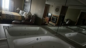A hotel bathroom with two large white tubs, a bed with a patterned bedspread, a television, and a mirror. - Super 8 by Wyndham Sparta (Sparta)