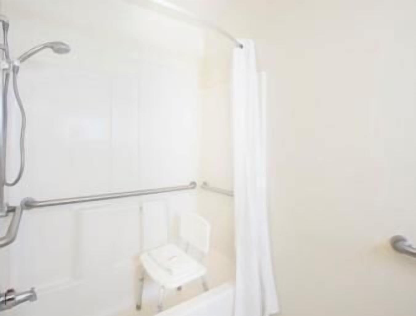 Une salle de bain avec une douche, un porte-serviettes et un petit tabouret blanc.