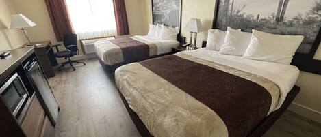 A hotel room with two beds, a desk with a lamp, a chair, and a large painting on the wall.