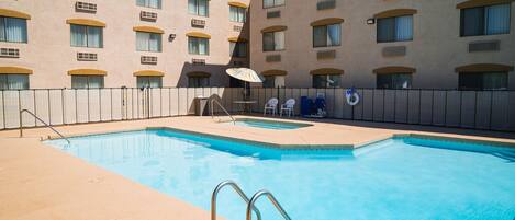 A swimming pool with a metal ladder, surrounded by a fence, and adjacent to a building with multiple windows and balconies.