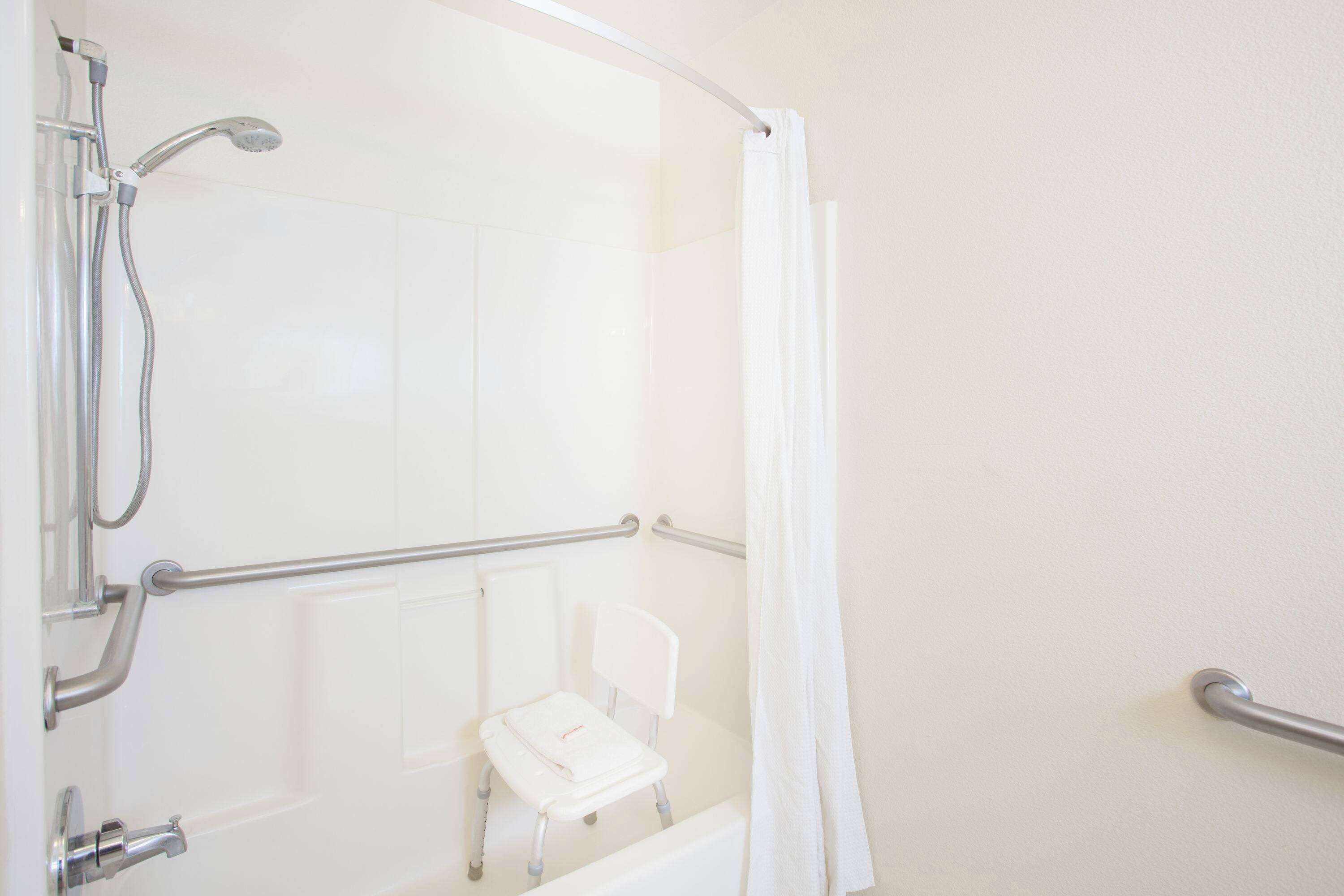 Un espace douche doté d’une porte en verre, d’une chaise blanche et de barres d’appui.