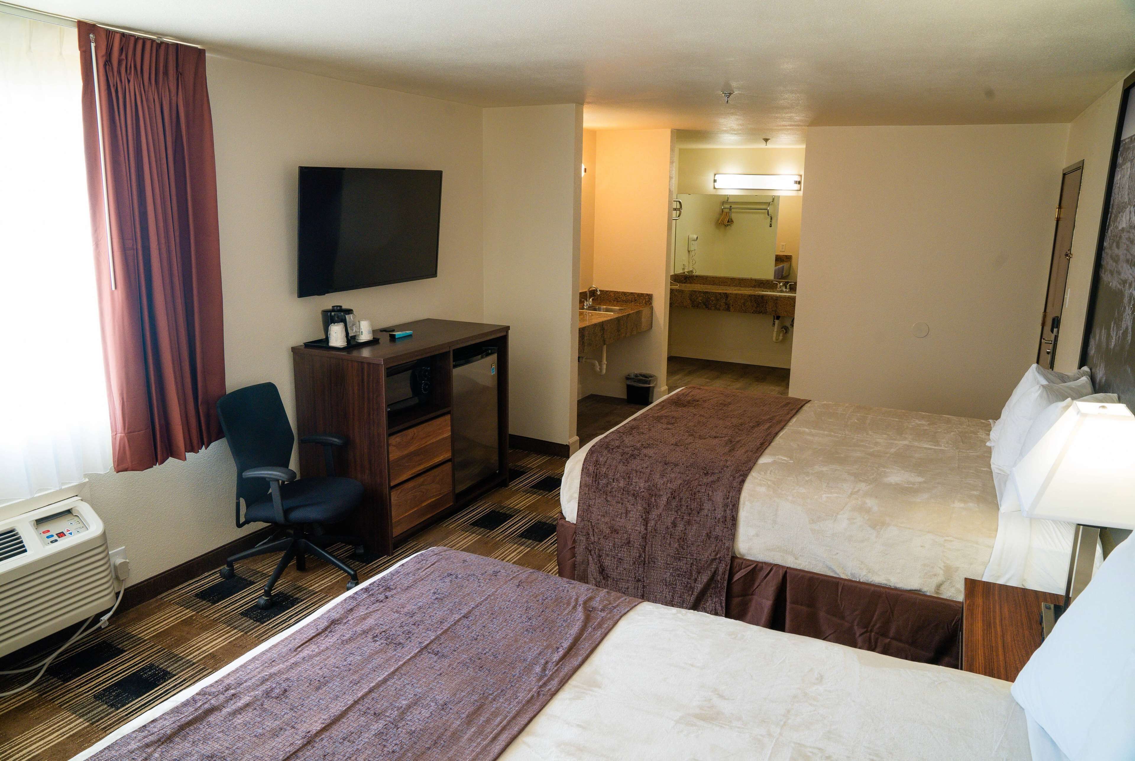 A hotel room with two beds, a desk, a chair, a TV, a bathroom visible through an open door, and a heater.