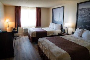 Quarto de hotel com duas camas, uma escrivaninha, uma cadeira e uma janela grande com cortinas.