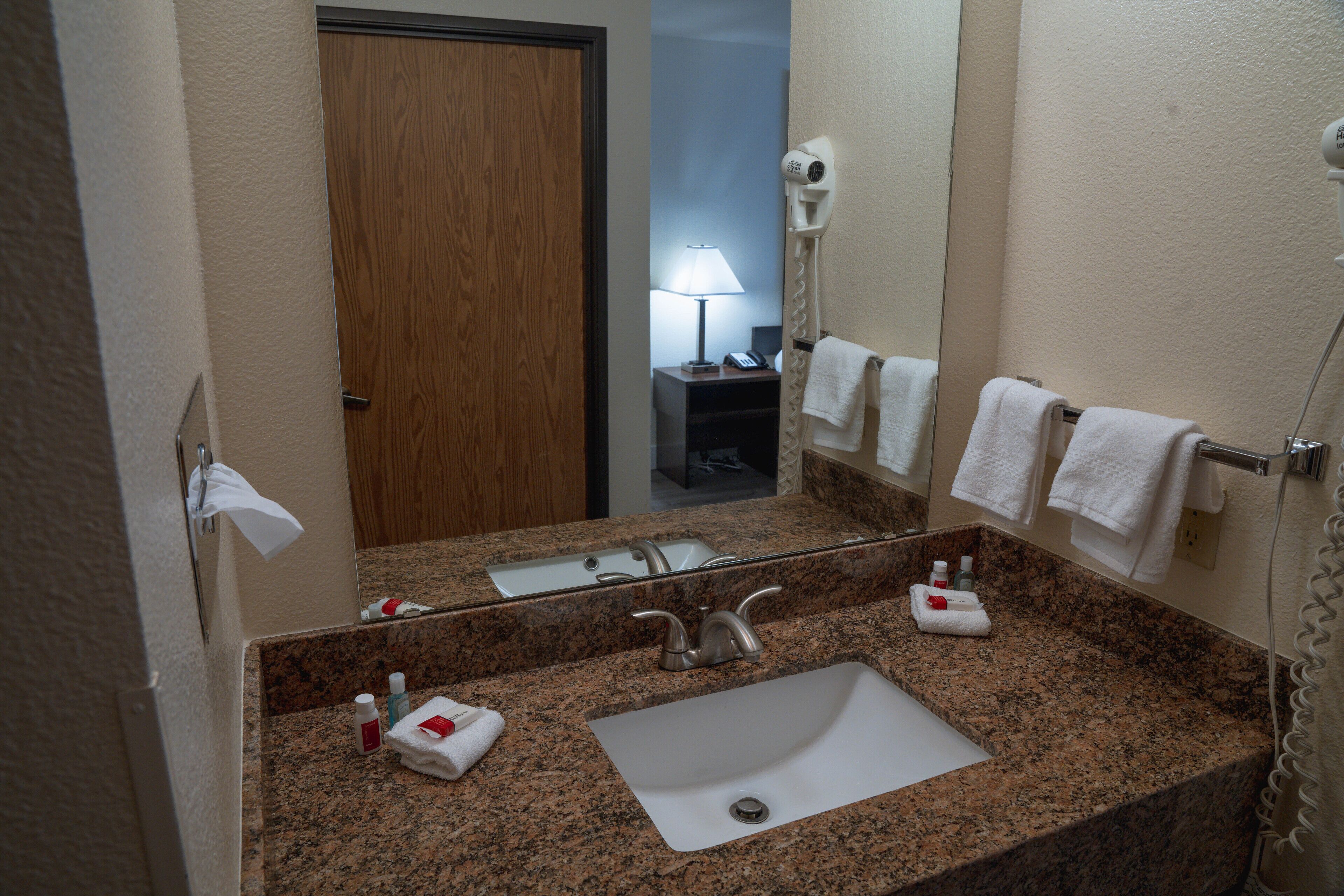 A bathroom with a granite countertop, a sink, a mirror, a towel rack, and a hairdryer.