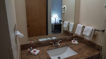 A bathroom with a granite countertop, a sink, a mirror, a towel rack, and a hairdryer.