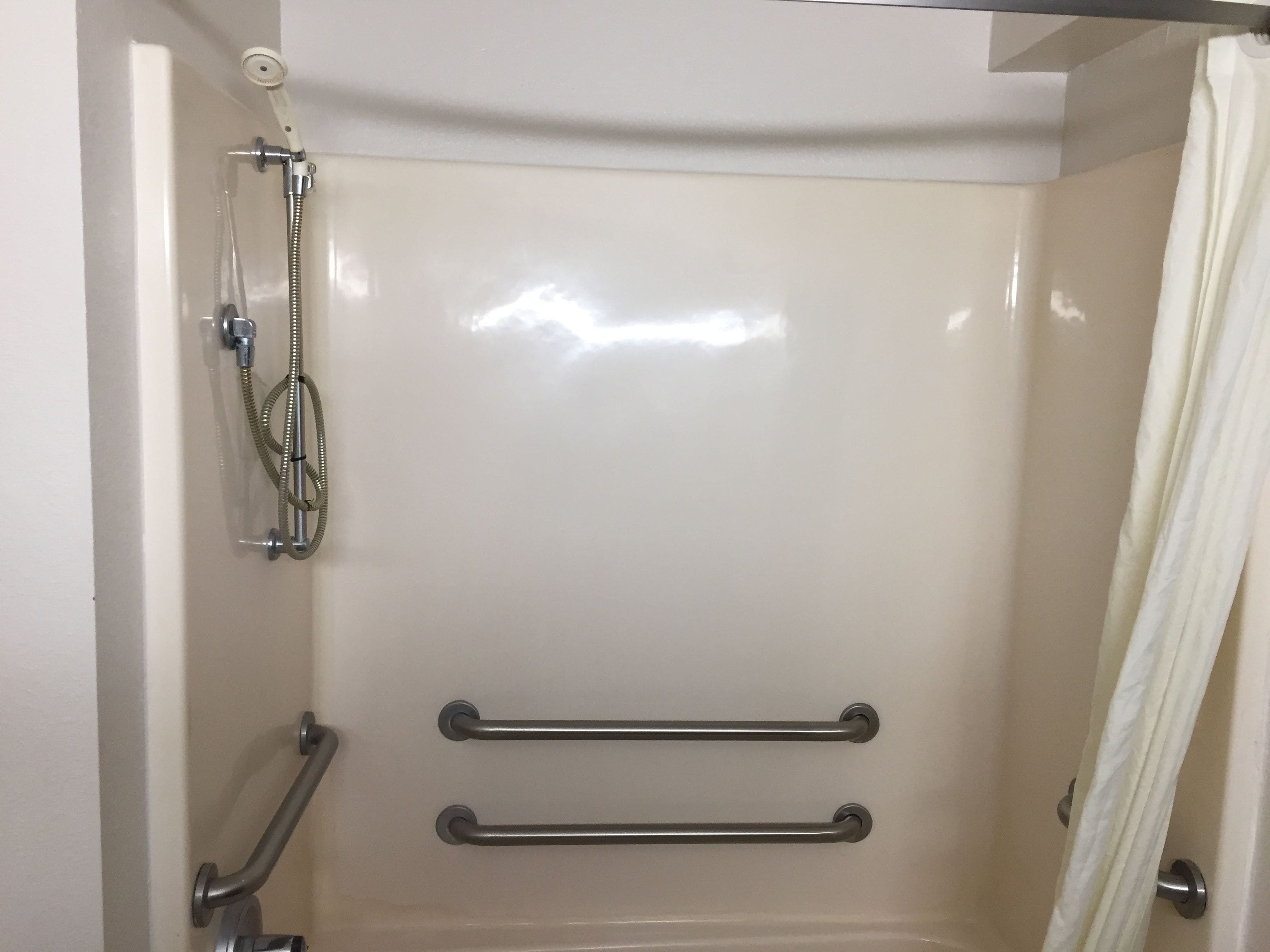 A shower with a handheld showerhead, grab bars, and a curtain.