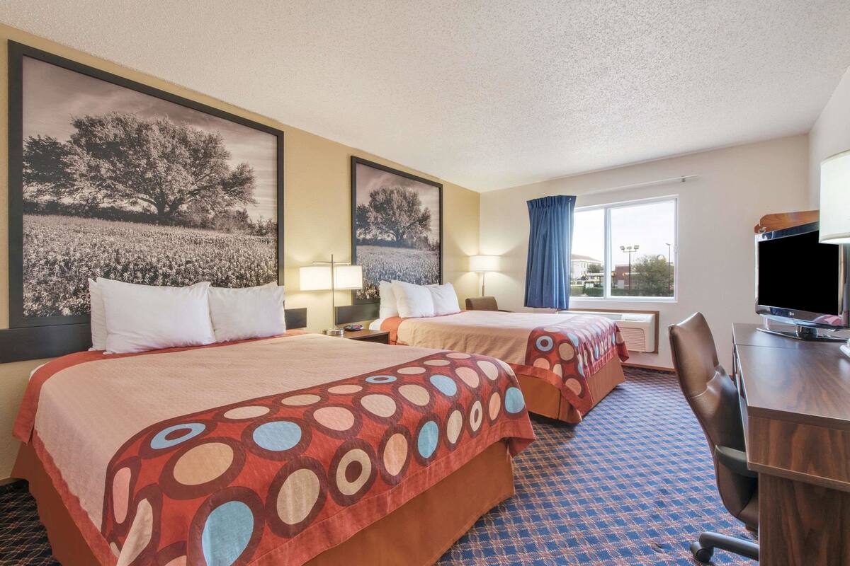 Ein Hotelzimmer mit zwei Betten, einem Schreibtisch, einem Stuhl und einem Fernseher.