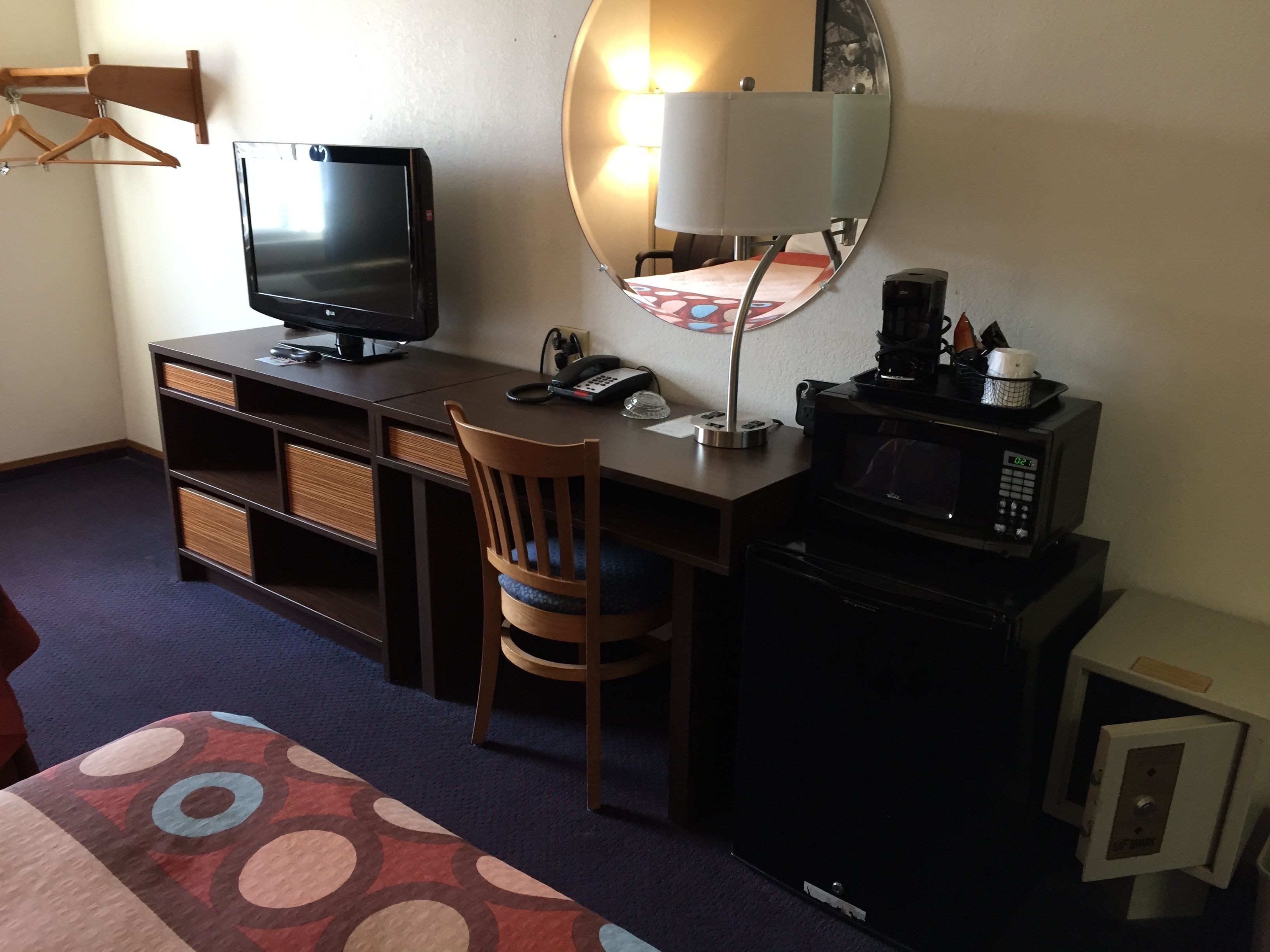 Une chambre d’hôtel équipée d’un bureau, d’une télévision, d’un four à micro-ondes, d’une chaise et d’un lit recouvert d’une couvre-lit à motifs.