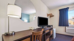 Een hotelkamer met een houten bureau, een televisie, een spiegel, een telefoon en een raam met gordijnen.