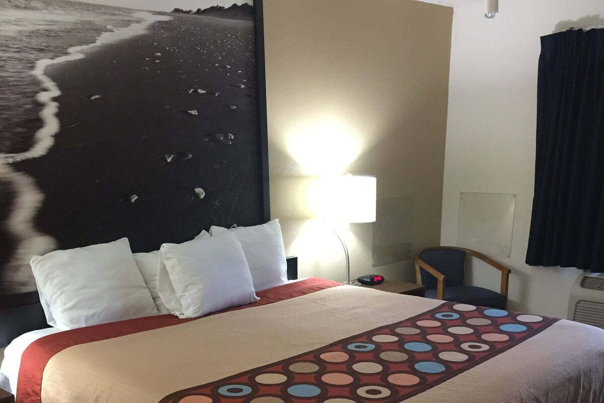 Ein Hotelzimmer mit Bett, Schreibtisch, Stuhl, Lampe und einem Bild an der Wand.