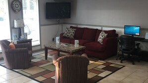 Een woonkamer met een rode bank, een salontafel, een televisie en een bureau.