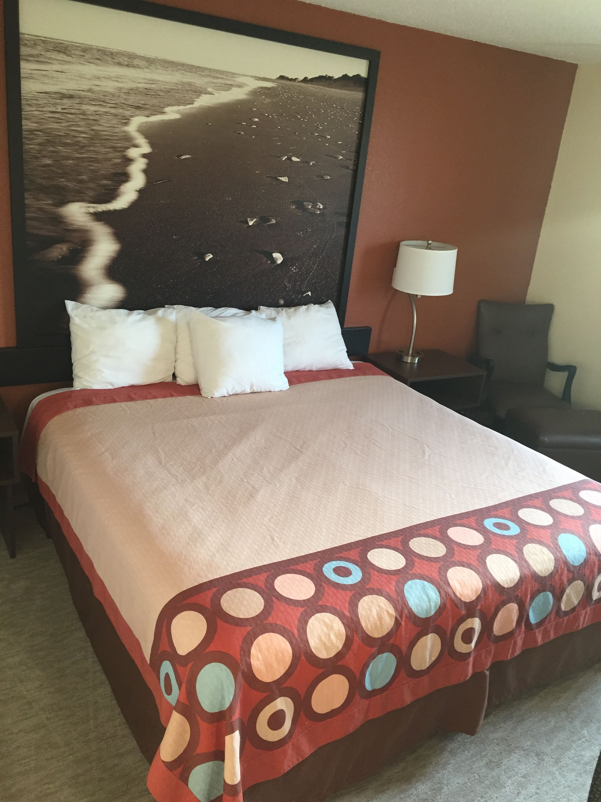 A hotel room with a large bed, a nightstand, a lamp, and a chair.