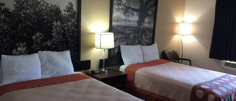 Habitación de hotel con dos camas, cada una con una colcha roja y blanca, una mesita de noche con lámpara y un cuadro grande enmarcado con un árbol.
