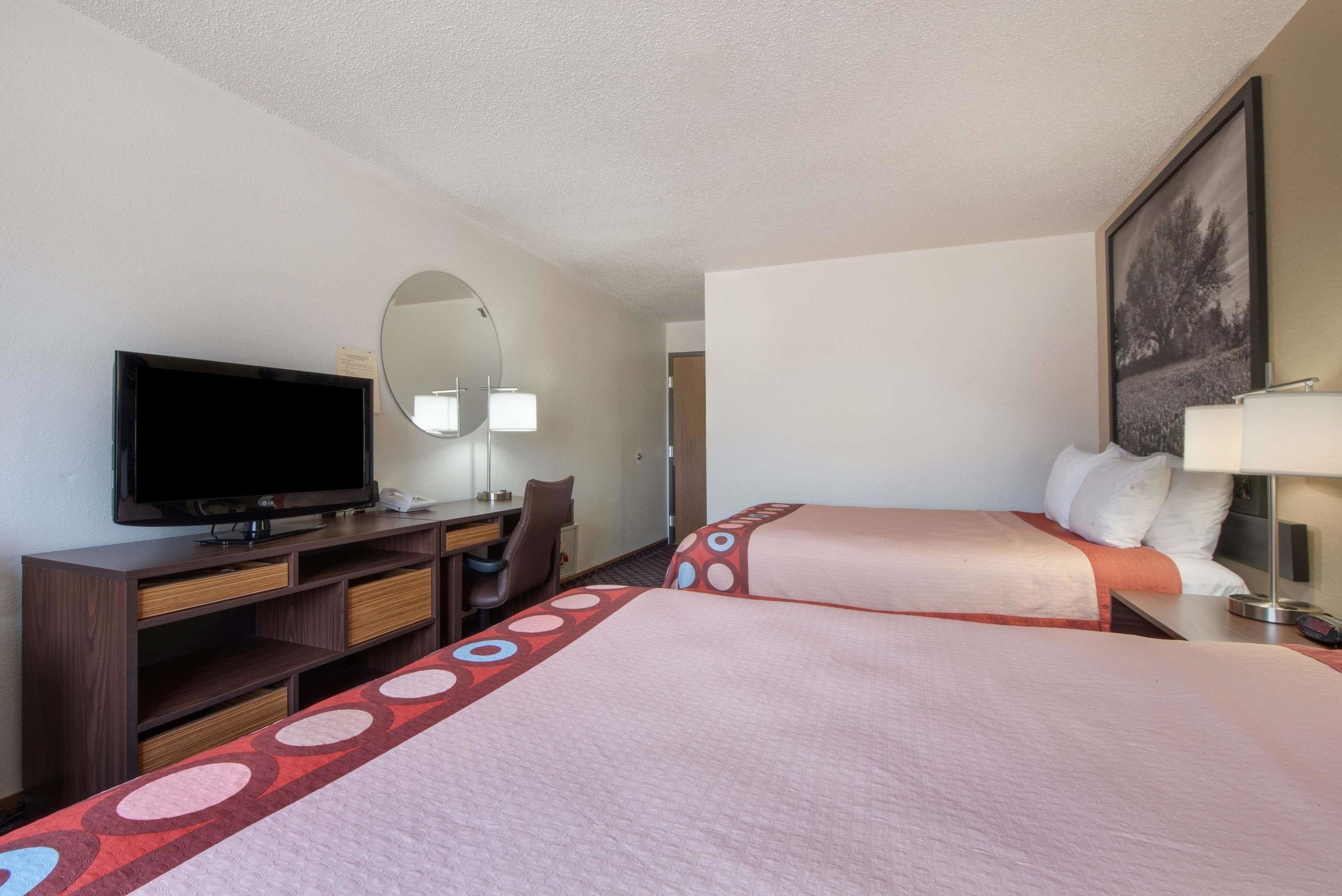 Habitación de hotel con dos camas, un escritorio, un televisor, una silla y un espejo.