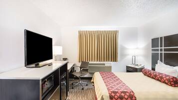 A hotel room with a TV, desk, chair, bed, and curtains.