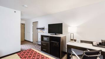 Une chambre d’hôtel comprenant un lit, un bureau avec un ordinateur, une télévision, un four à micro-ondes, un réfrigérateur, une chaise et une table de chevet.