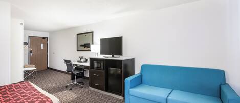 Habitación de hotel con cama, sofá azul, escritorio con computadora, televisor y minibar.