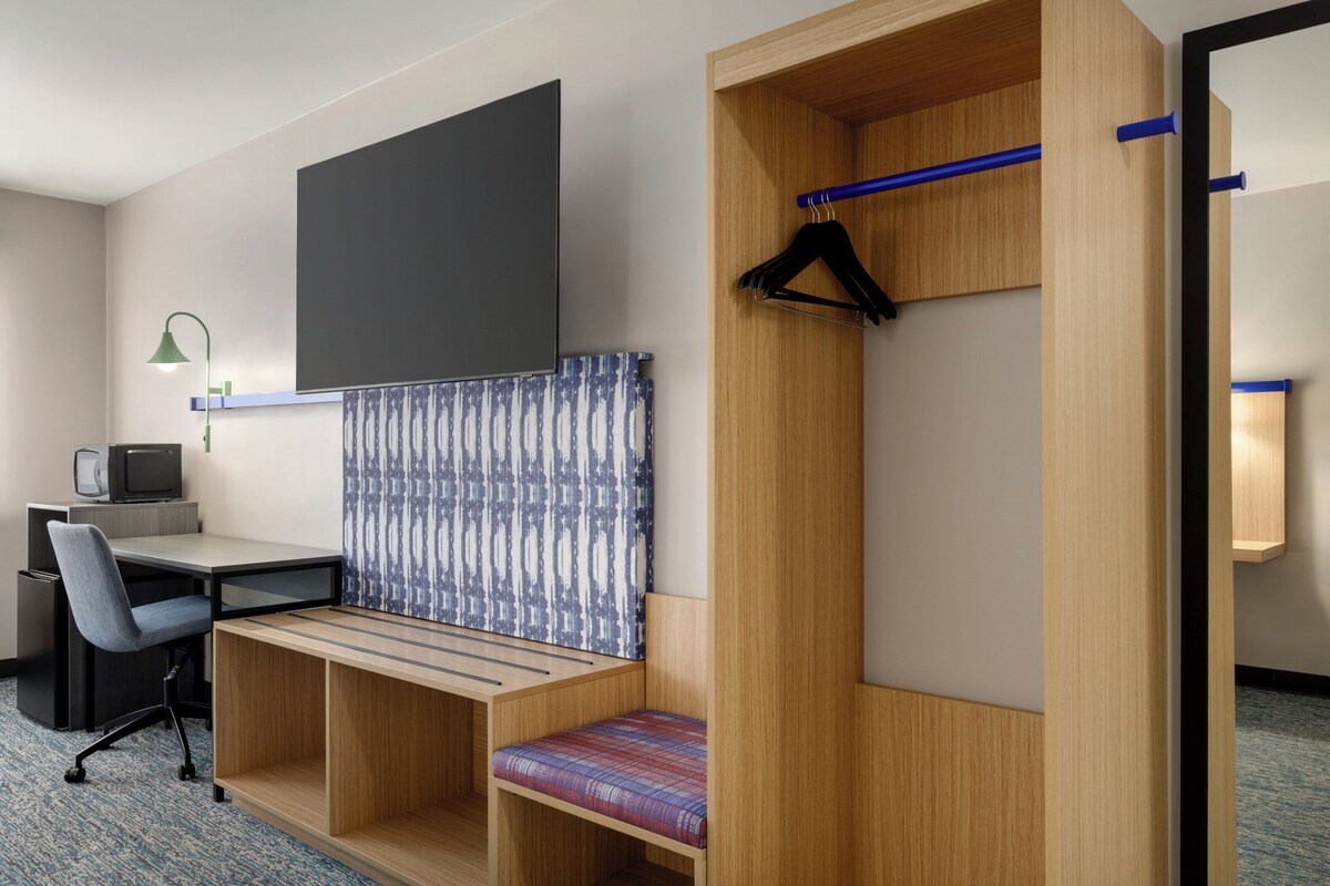 Habitación de hotel con escritorio, silla y un banco empotrado con cortina estampada.