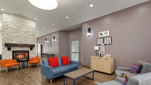 A modern living room with a stone fireplace, two orange armchairs, a blue sofa with red cushions, a wooden coffee table, and a wooden cabinet. - Garner Hotel Salt Lake City Airport by IHG (Salt Lake City)