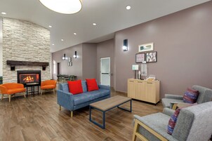 A modern living room with a stone fireplace, two orange armchairs, a blue sofa with red cushions, a wooden coffee table, and a wooden cabinet.