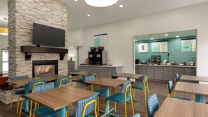 A modern restaurant with stone walls, a fireplace, and blue and yellow chairs. - Garner Hotel Salt Lake City Airport by IHG (Salt Lake City)