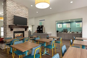 A modern restaurant with stone walls, a fireplace, and blue and yellow chairs.
